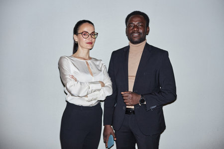 Two happy diverse corporate employees standing against light background looking at camera, medium long shotの写真素材