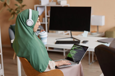 Side view portrait of Muslim young woman as female programmer writing code and wearing headscarf in office, copy spaceの写真素材