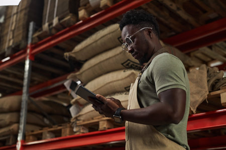 Side view portrait of young African American man holding digital tablet at warehouse in coffee...