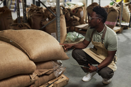 Side view portrait of Black young man inspecting coffee bags in warehouse while working in artisanal roastery, copy spaceの写真素材