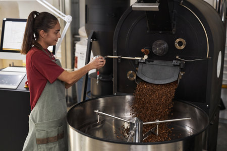Side view portrait of smiling young woman operating coffee roaster in workshop, copy spaceの写真素材