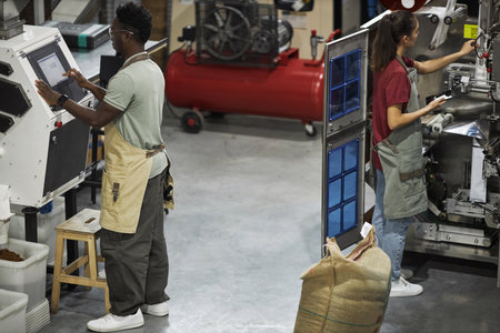 Two young people operating machines in food factory workshop, coffee production, copy spaceの写真素材