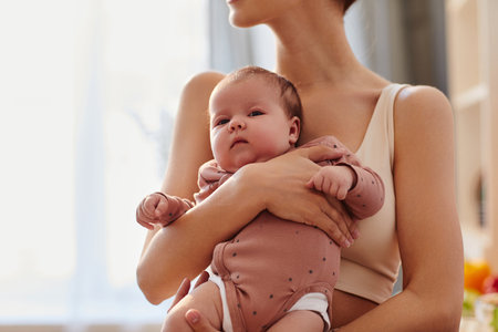 Cropped shot of peaceful baby girl in pink bodysuit looking at camera while sitting in arms of young mother, copy spaceの写真素材