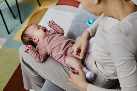 Top down shot of crying baby dressed in pastel bodysuit lying on mom lap, copy space