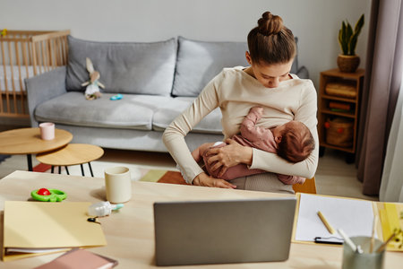 Medium shot of young woman breastfeeding infant while sitting at home officeの写真素材