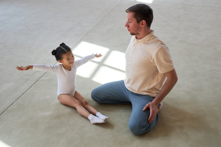 High angle view of happy Asian girl gymnast practicing exercises on gym floor while male coach observing accuracy of her movementsの写真素材