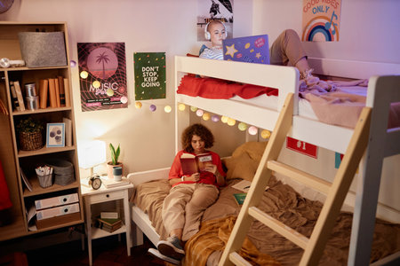 Portrait of two female college students enjoying relaxing evening on bunk bed in dorm room, copy spaceの写真素材
