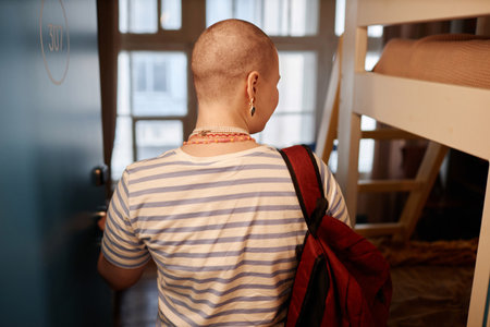 Back view of bald young woman opening door and entering college dorm room, copy spaceの写真素材