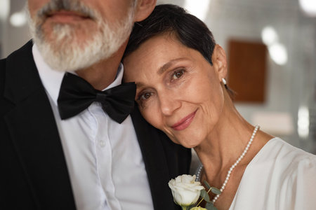 Close up portrait of beautiful senior woman as bride laying head on grooms shoulder and smiling at cameraの写真素材