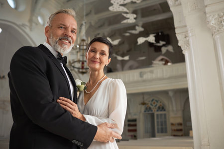 Waist up portrait of happy senior bride and groom looking at camera in church with smiles after wedding ceremony, copy spaceの写真素材