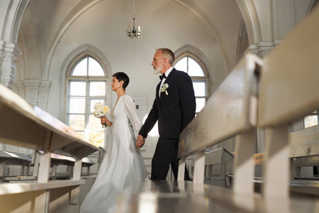 Side view portrait of senior couple walking together down church aisle on wedding day, copy spaceの写真素材