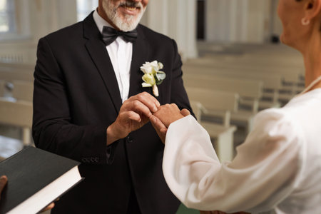 Closeup of senior groom exchanging rings with bride during wedding ceremony at churchの写真素材