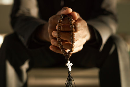 Closeup of priest holding wooden rosary beads and praying in ethereal sunlight, copy spaceの写真素材