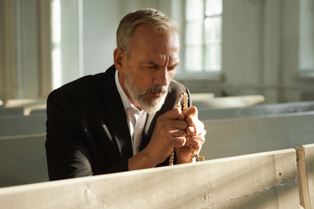 Portrait of bearded senior man praying in church and holding rosary beads, copy spaceの写真素材