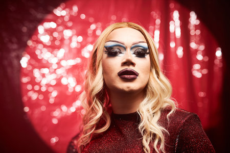 portrait of blonde drag queen performer on stage in spotlight against glittering red backgroundの写真素材