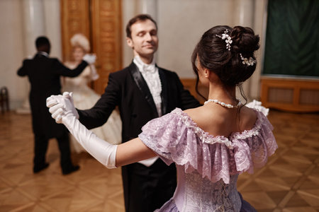 Back view of young lady wearing ballgown dancing waltz with gentleman in palace