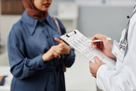 Cropped shot of male doctor filling medical card listening to female patient talking about symptoms of diseaseの写真素材