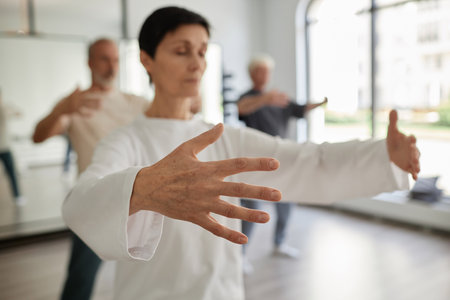 Medium shot with focus on hand of senior female student doing qigong concentration exercise in gymの写真素材