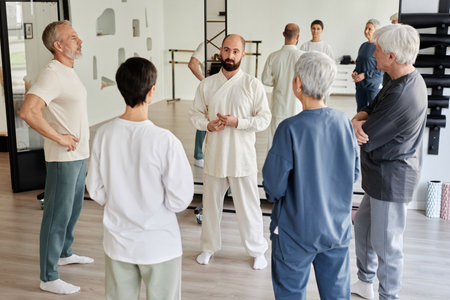 High angle view of elderly people looking at male master in white outfit explaining importance of qigong exercises for health, group back facing cameraの写真素材
