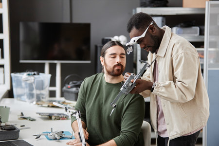 Portrait of two people inspecting action camera on drone in tech repair workshop, copy spaceの写真素材