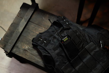 Above angle of black protective bulletproof body armor with walkie-talkie in pocket lying on wooden chest in military officeの写真素材