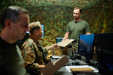 Young male officer in t-shirt passing folder with secret documents to multiethnic female colleague in camouflage uniformの写真素材