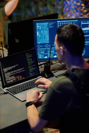 Young male military officer in uniform looking through data on laptop screen while sitting by...