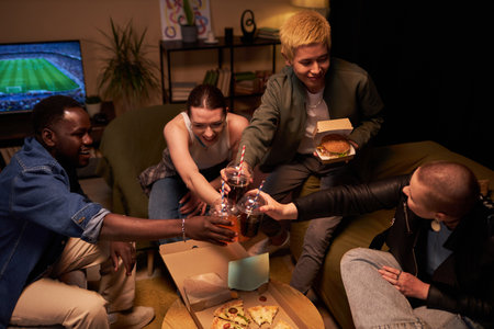 High angle shot of four multi-ethnic young students toasting with fizzy drinks while eating fast...