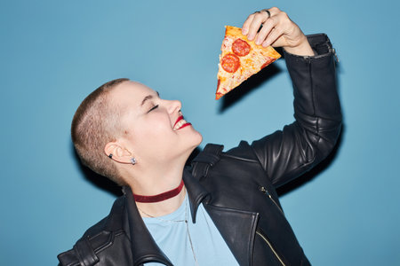 Medium close up shot of smiling young girl with buzz cut standing with eyes closed holding tasty...