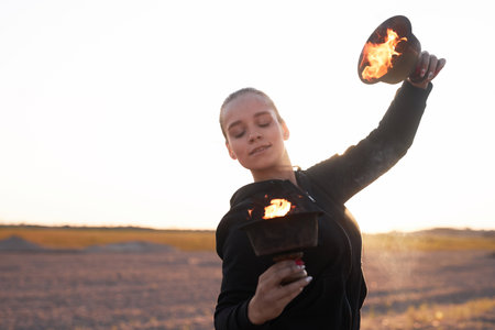 Waist up portrait of young woman dancing with flame bowls during fire show performance outdoors on...