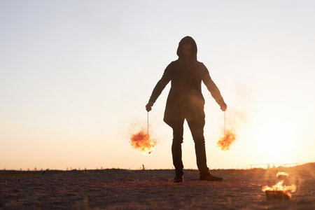 Full length portrait of young man holding fire poi during fire show performance in nature against sky, copy spaceの写真素材