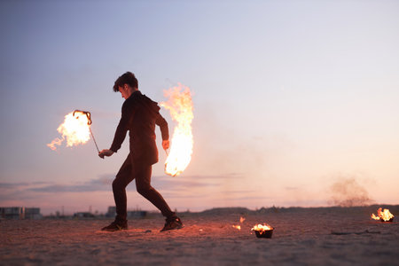 Full length side view of male fire show performer dancing with flames in nature during sunset, copy spaceの写真素材