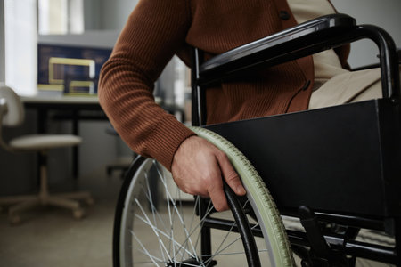 Close up of unrecognizable man with disability using wheelchair in office focus on hands turning wheel, copy spaceの写真素材