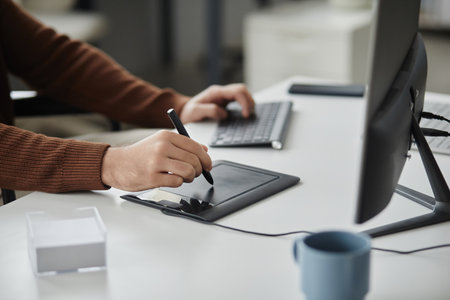 Close up of unrecognizable man using pen tablet for editing photos or videos at desk in office, copy...