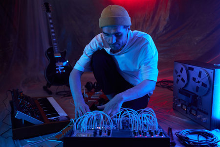 Medium full shot of male composer in blue neon light adjusting portable sound mixer for recording...