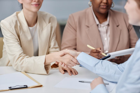 Cropped shot of unrecognizable business women shaking hands reaching agreement while sitting at desk in officeの写真素材