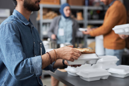 Side view closeup of unrecognizable Middle Eastern man volunteering at soup kitchen and giving free...
