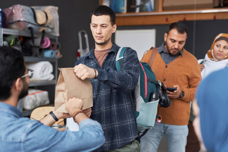 Waist up portrait of young man standing in line at refugee help center receiving food and donationsの写真素材