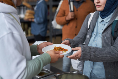 Close up of volunteer giving free hot meals to refugees at soup kitchen, focus on hands holding plateの写真素材
