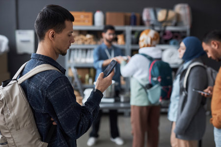 Side view portrait of young man with backpack holding smartphone and checking news and messages standing in refugee help center, copy spaceの写真素材