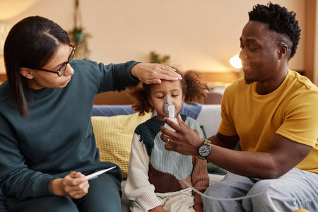 Medium long shot of family at home, mom measuring African American daughters temperature while father holding nebulizer mask at childs faceの写真素材