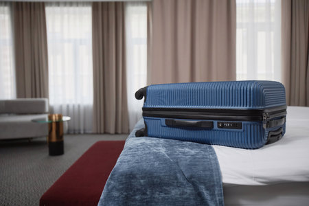 Side view background image of blue plastic suitcase on bed in luxury hotel room interior, copy spaceの写真素材