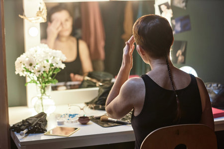 Back view of female artist doing make up by vanity mirror backstage in theater preparing for performance, copy spaceの写真素材
