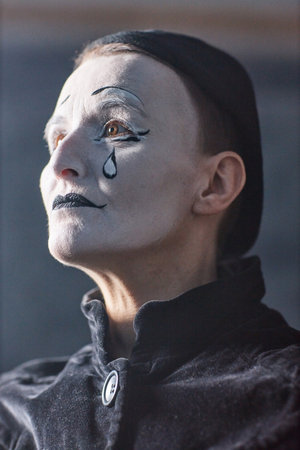 Dramatic vertical portrait of mime artist performing on stage in spotlight and looking up with tear make upの写真素材