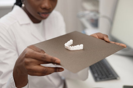 Close up shot of printed 3D lower jaw bone model on aluminum print bed in hands of Black woman in engineering laboratoryの写真素材