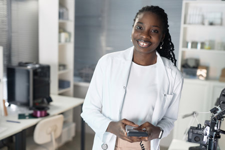 Waist up shot of cheerful African American female technician looking at camera while holding 3D printer controller in laboratoryの写真素材