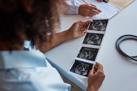 Over the shoulder of unborn baby ultrasonography picture in hands of African American woman at consultation in clinicの写真素材