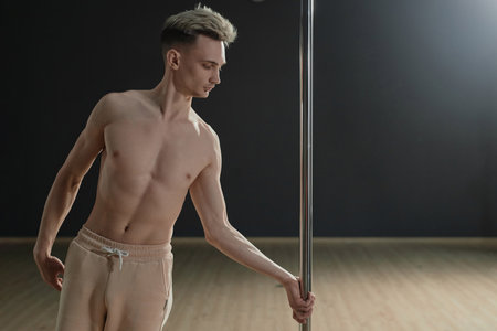 Medium long shot of bare-chested Caucasian man gripping pylon preparing for dance stunt in studioの写真素材