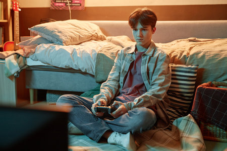 Portrait of teenage boy playing videogames sitting on floor at home, copy spaceの写真素材