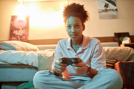 Portrait of teenage girl holding gamepad and playing videogames sitting on floor at home, copy space